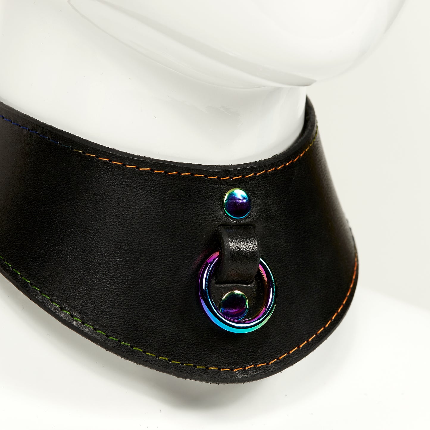 NAOMI COLLAR closeup 3/4 front view of wide, curved style collar in black leather with rainbow stitched edges, rainbow o-ring suspended from a strap tucked into collar, riveted with rainbow hardware