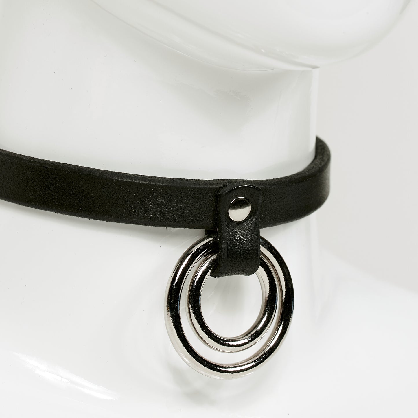 closeup 3/4 bview of slim leather choker on mannequin neck, with two concentric o-rings hanging from a strap rivited to main jewelry ERIN